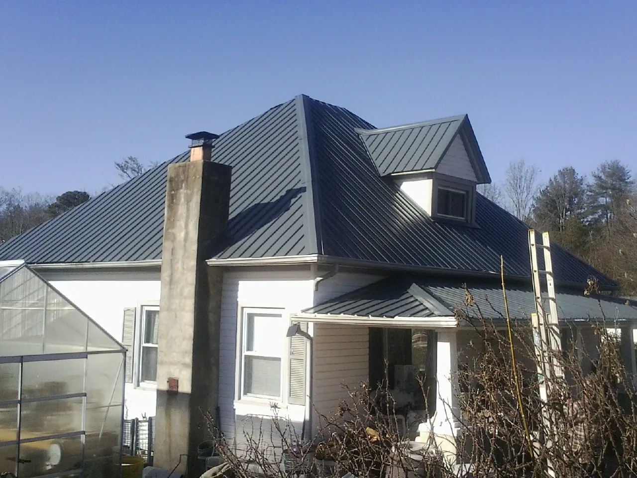 Dark blue standing seam metal roof on a white farmhouse with dormer — Slate & Tile Roof Repair by Roofing Brothers in Vinita