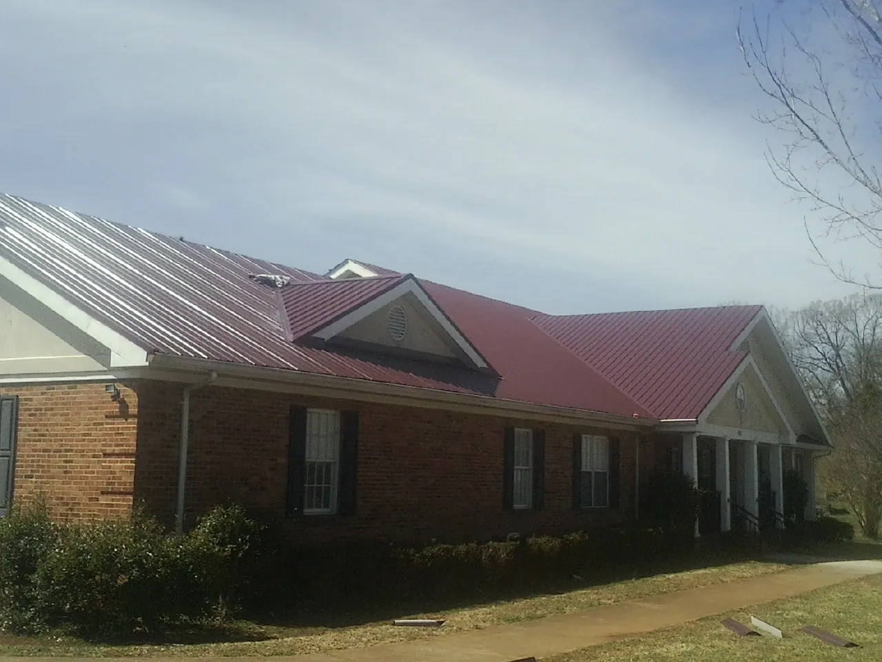 Red metal roof with gabled entries on a long brick building, from a Hail Damage Roof Repair job in Vinita