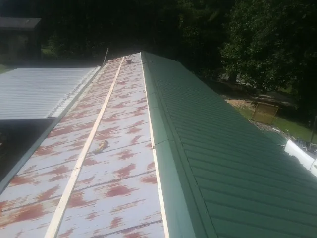 Old rusted panels beside newly installed green metal roofing — Wind Damage Roof Repair by Roofing Brothers in Vinita