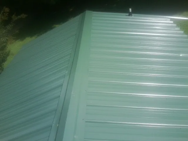 New green metal panels meeting at the ridge of a roof — Flat Roof Repair work by our crew in Vinita