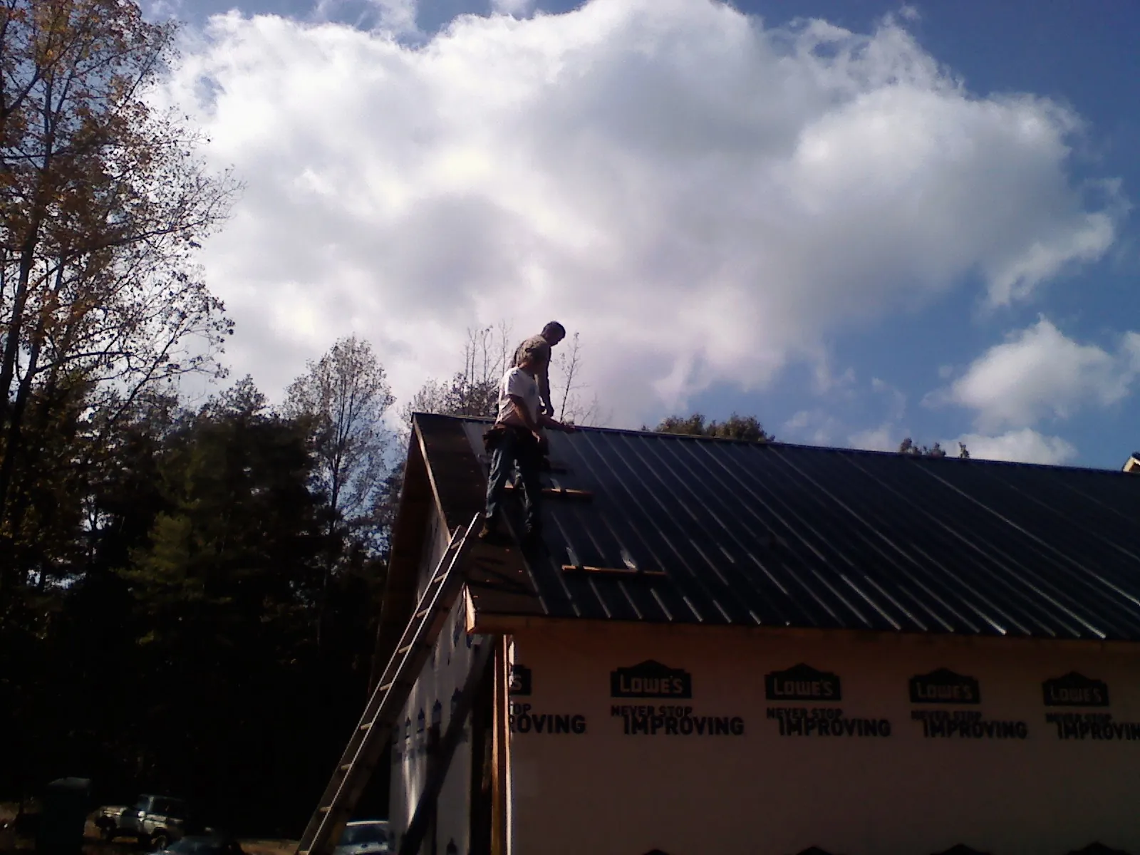 Roofer fastening dark metal panels high against a cloudy sky, from a Roof Inspection job in Vinita