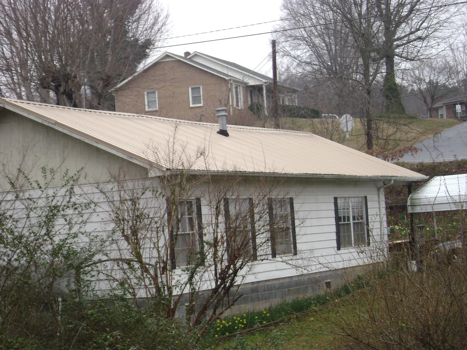 Tan metal roof on a white sided house set into a hillside — Commercial Roofing by Roofing Brothers in Vinita