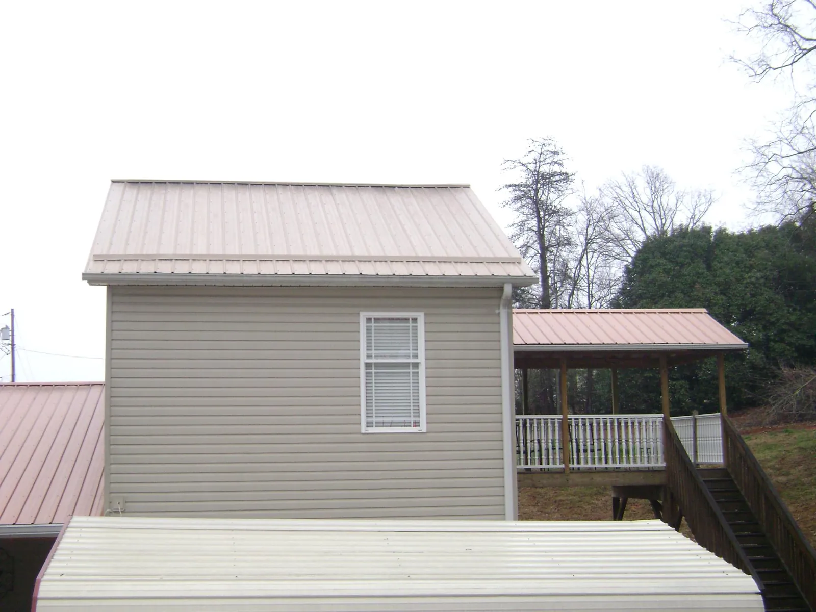Tan metal roofs on a two story addition and attached porch, from a Roof Replacement job in Vinita